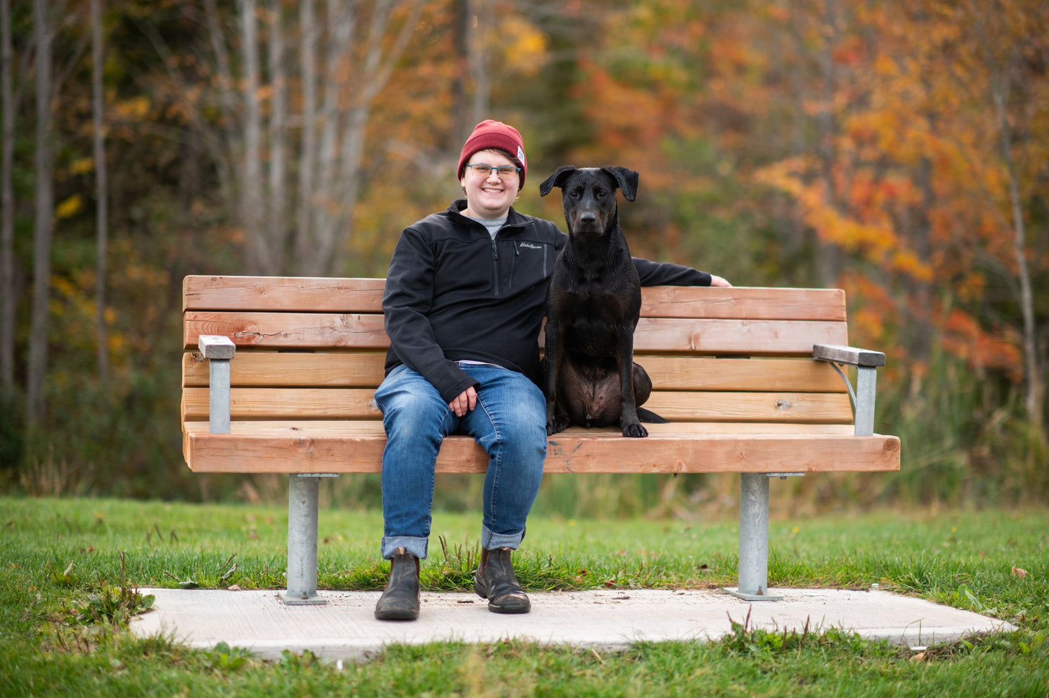 Person sitting on a bench with a black dog in an autumn park setting